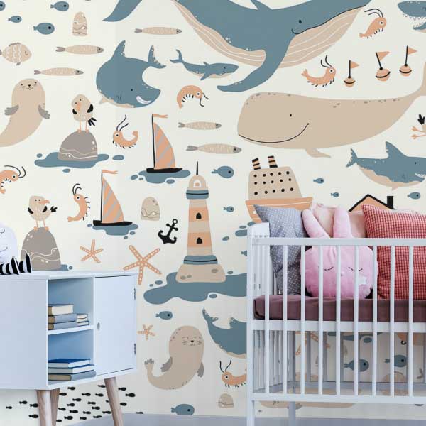 A cheerful nautical-themed mural perfect for nurseries, featuring smiling whales, sea creatures, sailboats, lighthouses, and stars in soft beige, blue, and peach. The room includes a white crib, plush cloud pillows, and a toy shelf, creating a cozy and playful ocean-inspired setting. The Fancy Walls peel and stick or non-pasted wallpaper is available in custom sizes for your wall.