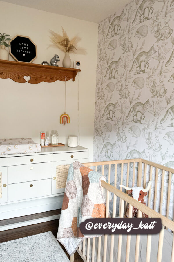 Fox, rabbit, and hedgehog patterned wallpaper complementing a minimalist nursery with warm wooden furniture and earthy accents