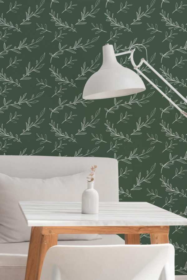 A green botanical wallpaper featuring delicate white line-art leaves arranged in a flowing, repeat pattern, adding organic movement and calm to the setting. The leafy design complements the minimalist white dining area, styled with a modern marble-top table, wooden legs, a soft gray couch, and a sculptural floor lamp. The Fancy Walls peel and stick or non-pasted wallpaper enhances modern café or home office interiors with its clean, nature-inspired aesthetic and calming color palette.