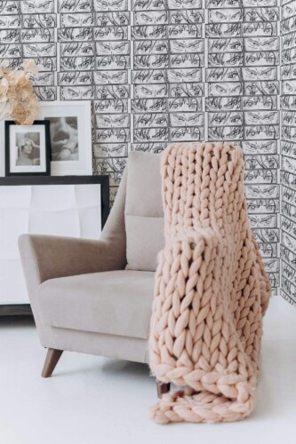 Anime abstract peel and stick wallpaper with black and white manga eyes in cozy reading nook with beige chair and chunky blanket