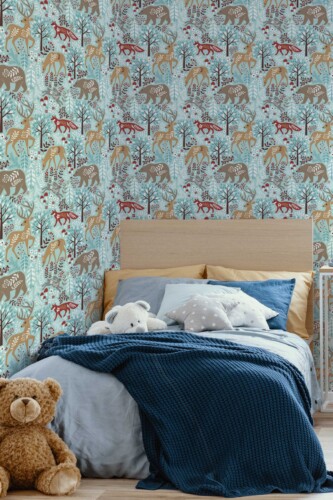 Children’s bedroom with a cozy bed draped in a dark blue throw blanket, set against an accent wall featuring a whimsical winter woodland wallpaper. The pattern displays illustrated deer, foxes, and other forest creatures in soft browns and reds, interspersed with blue and white foliage on a pale teal background. Plush teddy bears and pillows add warmth and comfort. The overall scene evokes a calm, storybook ambiance that blends playful animal motifs with soothing winter hues.