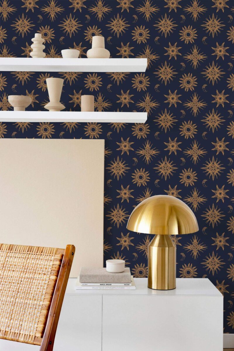 Celestial wallpaper featuring gold sun and moon motifs arranged in a symmetrical pattern across a deep navy background, styled in a modern room with minimalist décor. The Fancy Walls peel and stick or non-pasted wallpaper brings a bold, cosmic flair to a contemporary interior, complementing neutral ceramics, natural textures, and metallic accents. Ideal for accent walls in bedrooms, home offices, or creative studios.