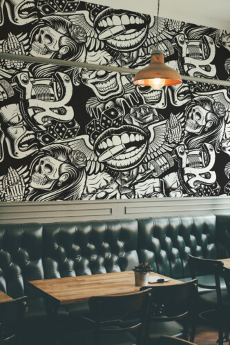 Graffiti Tattoo Art Wall Mural with black-and-white tattoo-inspired street art featuring skulls, clowns, lips, bullets, and wings, ideal for barber shops or urban interiors.