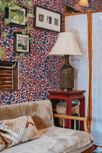 Cozy eclectic living space featuring Fancy Walls “Patriot Wildcat Print” wallpaper, styled with a bold animal-inspired pattern in rich red, navy blue, and white. The cheetah-like spots create dynamic visual movement, wrapping the walls in a lively, modern rhythm. Paired with a velvet sofa, vintage red side table, sculptural lamp, and black-and-white photography, the design adds a vibrant twist to a retro-meets-artful interior. Available in peel and stick or non-pasted PVC-free wallpaper, printed with eco-safe GreenGuard Gold certified inks.
