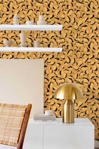 Interior scene showcasing a bold orange-and-black cheetah print wallpaper behind sleek white shelving. Each shelf holds minimalist ceramic vases in neutral tones. A modern white sideboard beneath the shelves displays a blank canvas, while a shiny brass lamp adds an elegant accent. On the left, a natural rattan chair contributes warmth and texture. The lively animal print wallpaper creates a dynamic focal point, contrasting beautifully with the clean lines and calming neutral décor.