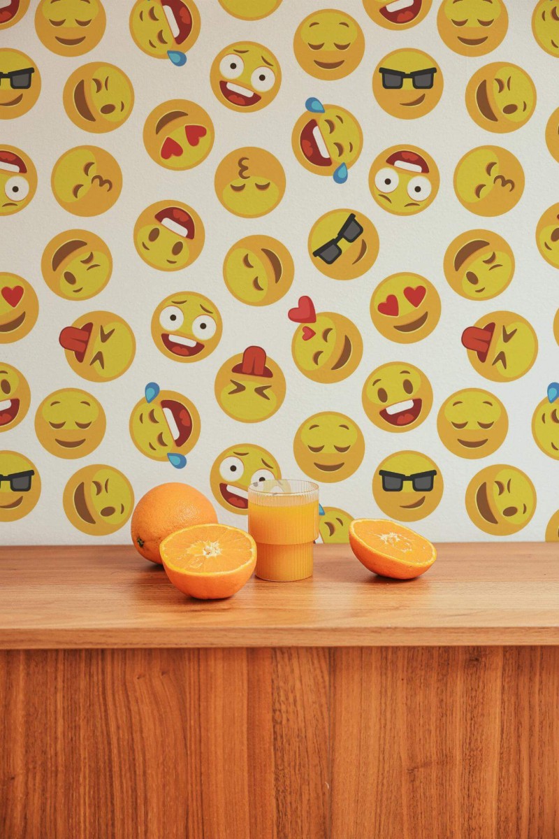 Emoji Wallpaper featuring bright yellow emoticons with various expressions on a white background, styled above a wooden counter displaying fresh orange slices. The cheerful design adds a playful, modern accent to the space.