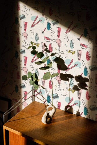 A colorful novelty wallpaper featuring beauty salon tools like hairdryers, combs, flat irons, and cosmetics drawn in a playful illustrated style on a light background. The wallpaper adds charm and energy to this powder room or salon interior, enhanced by warm natural light and mid-century modern décor. The Fancy Walls peel and stick or non-pasted wallpaper makes this vibrant design easy to apply, offering a durable and stylish solution for personal or professional spaces.