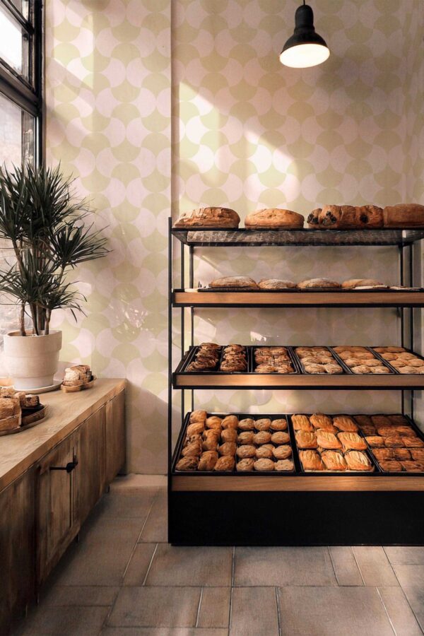 Warm bakery interior featuring wooden display shelves and Cozy Coffee Shop Classic wallpaper in the background. The light sage tile pattern brings balance and charm to rustic or artisan-inspired commercial spaces.