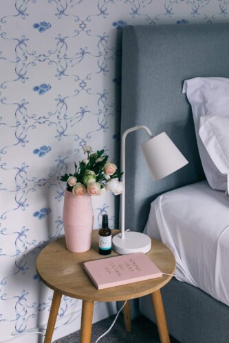 This delicate wallpaper features a soft blue floral design with ribbons, creating a charming and tranquil atmosphere for the room. The pale blue roses and whimsical ribbons dance across the wallpaper in a seamless, repeating pattern. It pairs beautifully with light, modern furniture, such as the minimalist nightstand and soft bedding, adding a serene, sophisticated touch to the space. The Fancy Walls peel and stick or non-pasted wallpaper brings a refined, feminine elegance to any bedroom or living area.