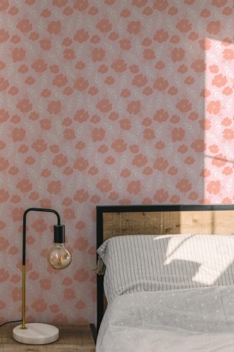 Aesthetic hibiscus floral wallpaper in soft pink tones features a repeating pattern of stylized hibiscus blossoms and delicate white botanical leaves. The floral wallpaper creates a peaceful, feminine ambiance in this sunlit bedroom, styled with a wooden headboard, striped bedding, and a modern marble-based lamp. Ideal for nurseries, bedrooms, or cozy corners, this design is available as Fancy Walls peel and stick or non-pasted wallpaper, made with PVC-free materials and GreenGuard Gold certified inks for vibrant color and safe indoor air.