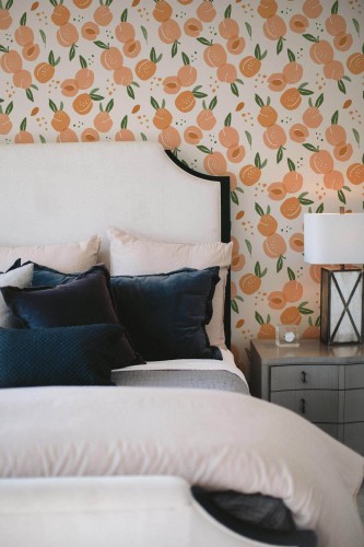 Peach Aesthetic wallpaper with hand-drawn peaches and green leaves on white, styled in a cozy bedroom with neutral bedding and velvet pillows.