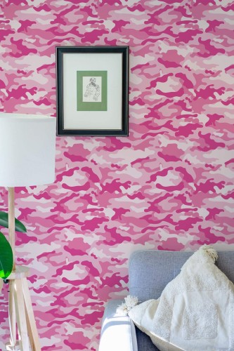Pink Camouflage Wallpaper with abstract pink, magenta, and blush shapes, styled in a bright living area featuring a light gray sofa, white floor lamp, and a framed illustration on the wall. The bold camo pattern adds playful energy and modern flair to the room.