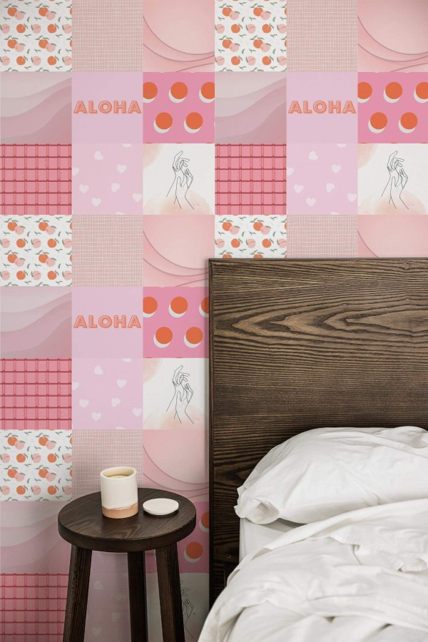Bedroom featuring a whimsical pink collage wallpaper composed of square tiles with varied patterns, including hearts, fruits, “Aloha” text, and minimalist line-drawn figures. The patchwork design layers soft pastel hues, geometric shapes, and playful prints to create a vibrant accent wall. A dark wooden headboard anchors the right side, complemented by crisp white bedding. A small round wooden nightstand with a simple white candle stands nearby, adding a cozy, modern contrast.