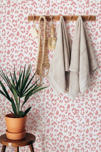 A pink leopard print wallpaper with soft mauve spots on a white background adds a trendy, playful touch to a bathroom interior. The eclectic animal pattern complements the natural tones of beige towels and a wooden stool with a terracotta plant, creating a stylish spa-like ambiance. This is a Fancy Walls peel and stick or non-pasted wallpaper, available in PVC-free materials for easy application or traditional paste installation.