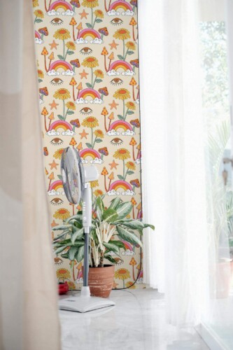 Retro Psychedelic Wallpaper featuring playful mushroom and floral motifs in warm oranges, yellows, and pinks on a soft pastel background, styled in a bright interior with sheer curtains, marble flooring, a modern standing fan, and a potted plant. The bold, vintage-inspired pattern adds a lively, bohemian accent to the room.