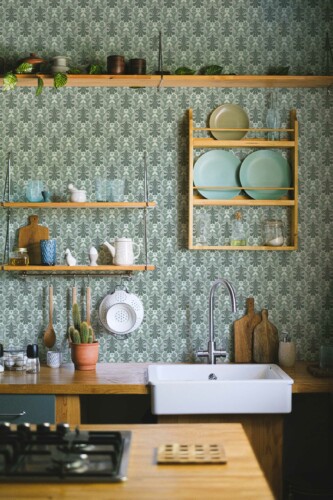 Cozy kitchen interior featuring Vintage Green Kitchen wallpaper in a classic damask pattern, paired with wooden open shelves, a white farmhouse sink, and potted succulents.