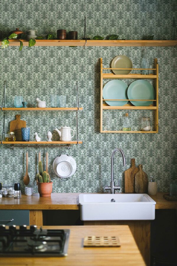 Cozy kitchen interior featuring Vintage Green Kitchen wallpaper in a classic damask pattern, paired with wooden open shelves, a white farmhouse sink, and potted succulents.