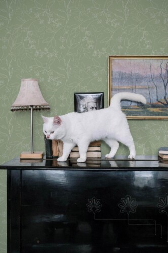 Sage green leaf peel and stick wallpaper in botanical style bedroom with white cat, vintage lamp, and framed artwork