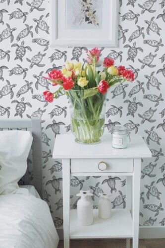 Sea Turtles Wallpaper in a detailed black-and-white turtle motif, styled in a bright bedroom with a white nightstand holding a vase of colorful tulips and minimalist decor. The nautical-inspired design adds a tranquil, nature-focused accent to the space.