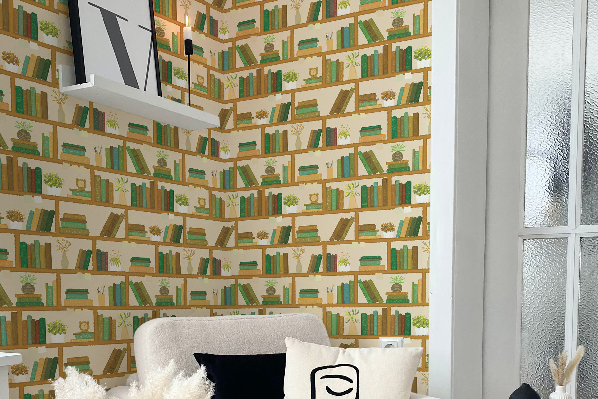 Reading nook with cozy armchair and illustrated bookshelf wallpaper filled with green and brown books and plants – eco-friendly removable wallpaper.