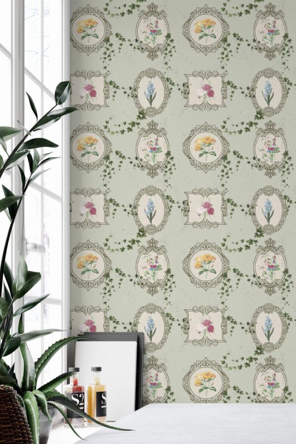 Dollhouse Garden Wallpaper with soft green background, vintage-style floral frames, and scattered ivy motifs, styled in a bright interior corner with large windows and a minimal white tabletop. The whimsical botanical design adds nostalgic charm and a delicate pop of color to the space.