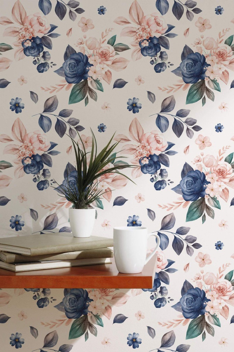 Pink and Navy Floral Wallpaper featuring delicate pink roses and deep navy blooms with lush foliage on a soft white background, styled in a serene space with a simple wooden shelf, a potted plant, stacked books, and a white mug. The botanical pattern adds a warm, elegant touch to the room.