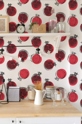 Vibrant pomegranate wallpaper featuring red and black fruit outlines on a crisp white background, displayed in a bright kitchen with a wooden countertop, open shelves, and minimal decor.