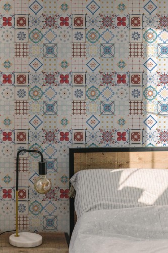 Portuguese Tile wallpaper with multicolor vintage-style tile pattern, styled in a sunlit bedroom with wood bedframe and modern lamp.