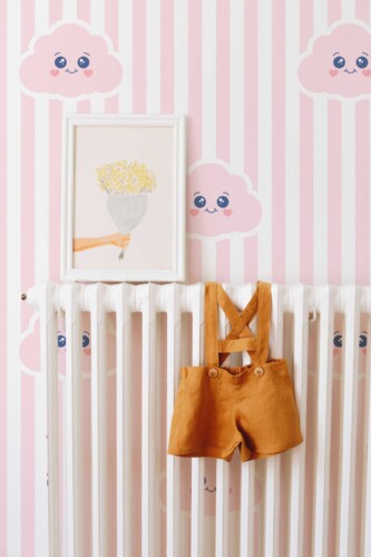 Fancy Walls peel and stick wallpaper with smiling pink clouds and soft stripes for a cute pastel nursery look.
