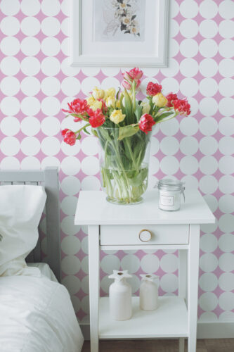 Bold Retro Polka Dot peel and stick wallpaper with oversized white circles on a pink wall behind a bedside table.