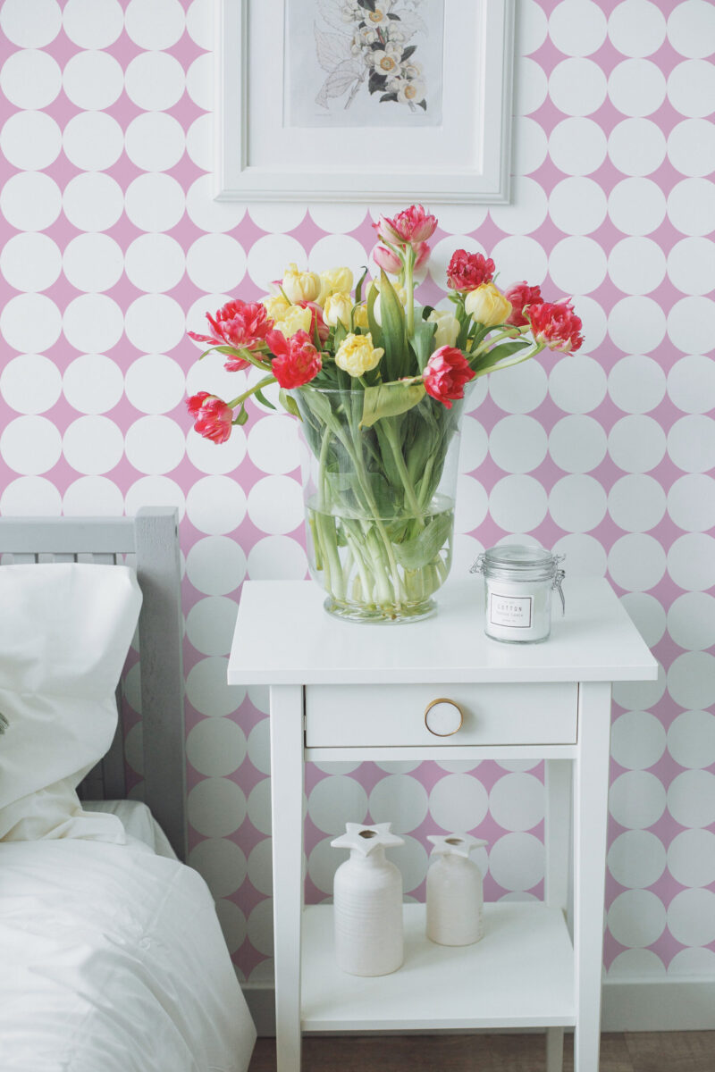 Bold Retro Polka Dot peel and stick wallpaper with oversized white circles on a pink wall behind a bedside table.