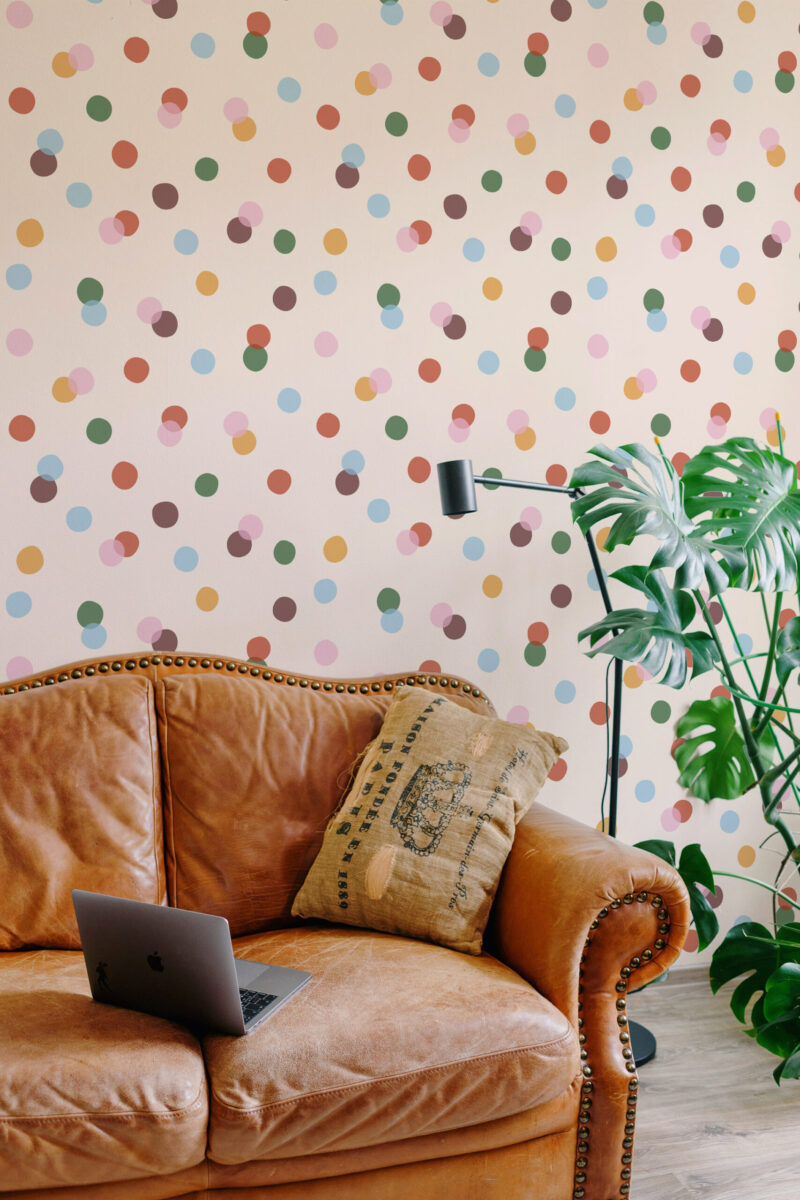 Vintage Colorful Polka Dot peel and stick wallpaper covering a living room wall behind a leather sofa with a floor lamp nearby.