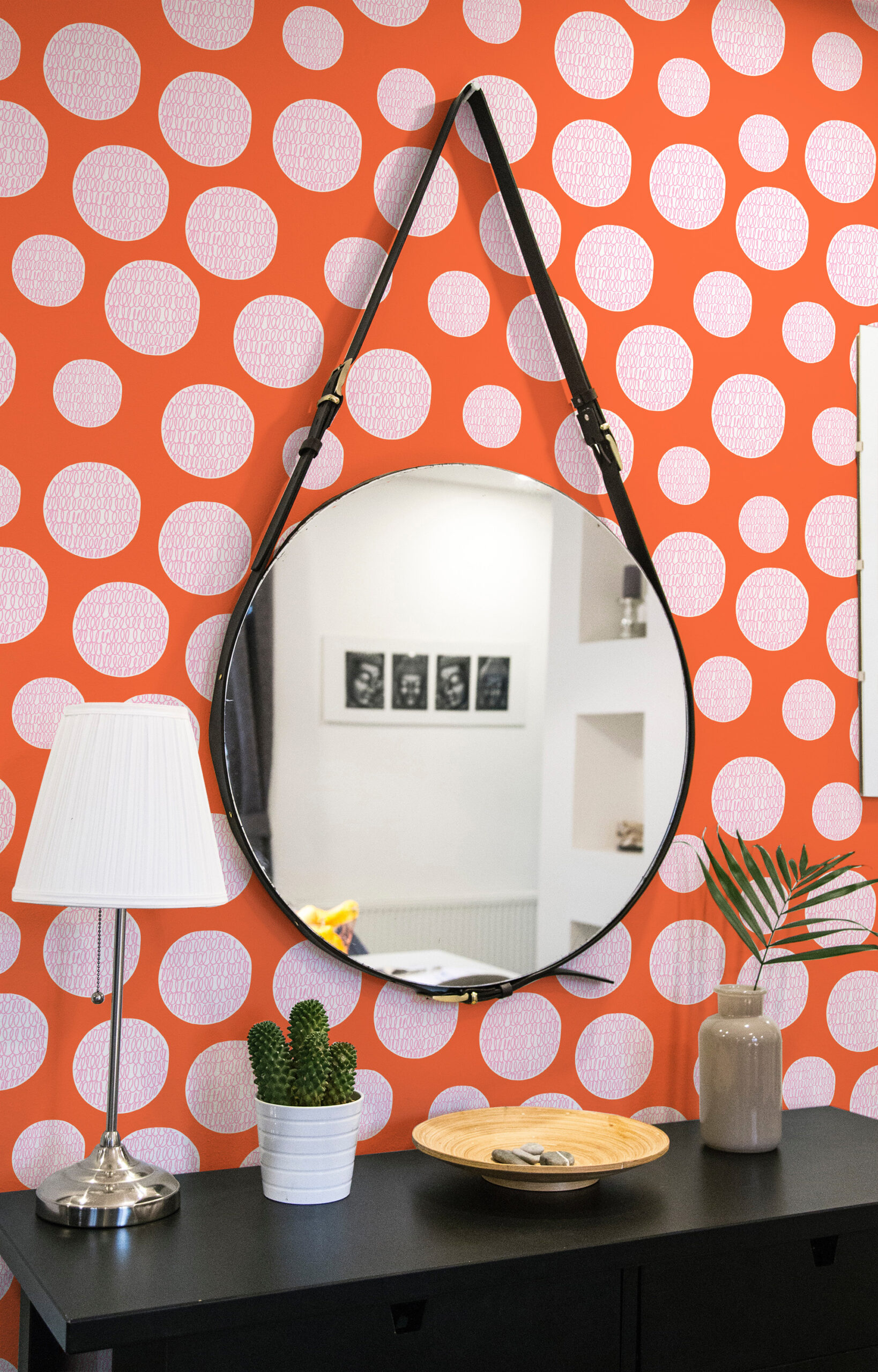 Bold Orange Scribble Dot peel and stick wallpaper with scattered pale pink dots on an orange wall behind a round mirror.