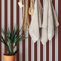 Bold Maroon Striped peel and stick wallpaper with vertical maroon, cream, and pale blue lines behind a wooden towel rack.