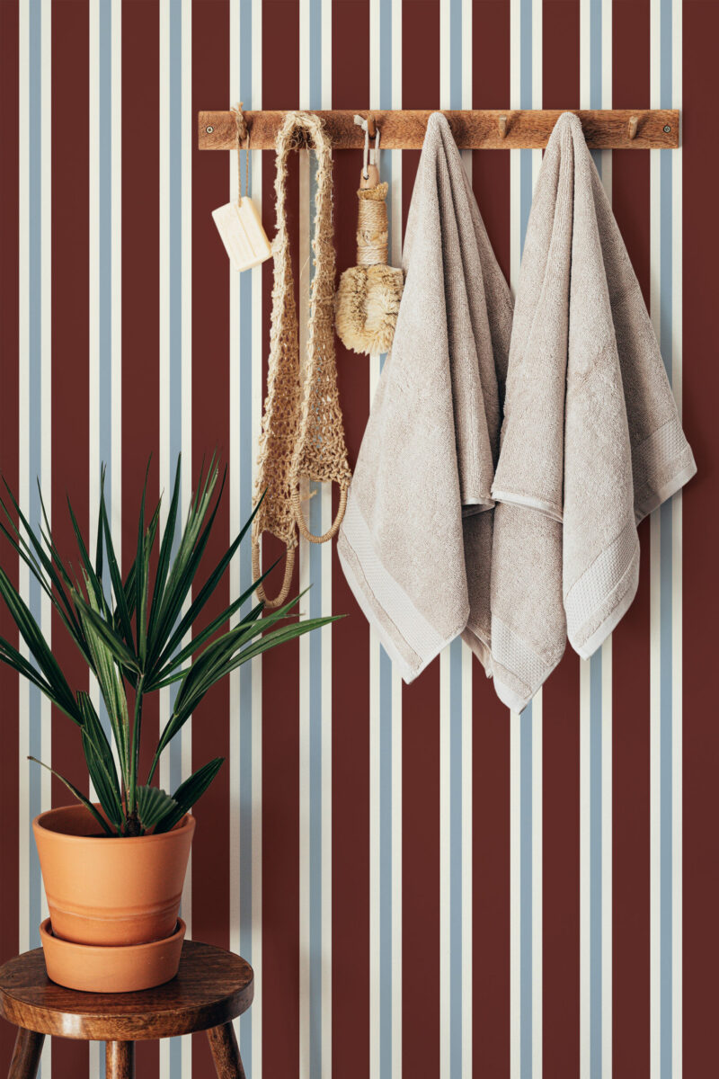 Bold Maroon Striped peel and stick wallpaper with vertical maroon, cream, and pale blue lines behind a wooden towel rack.