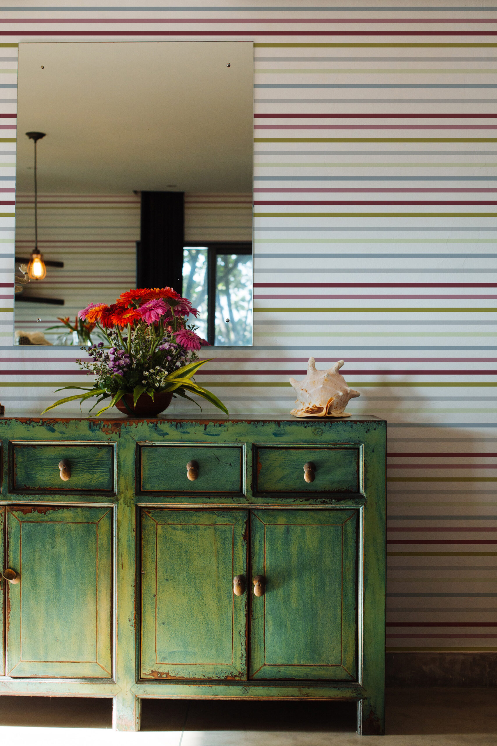 Fine Colorful Stripe adds thin multicolor horizontal lines as non-pasted wallpaper behind a mirror and a distressed green cabinet.