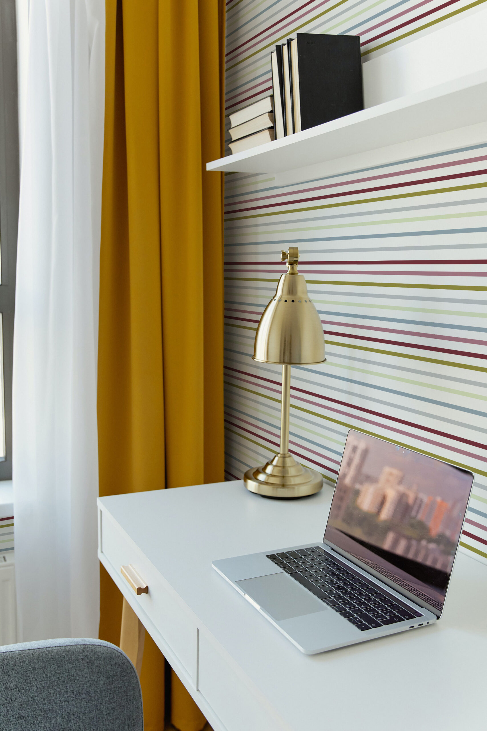 Fine Colorful Stripe self-adhesive wallpaper with thin multicolored horizontal lines behind a desk and lamp.