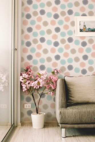 Spaced Beige Dots peel and stick wallpaper in soft pastel circles on a wall beside a sofa in a living room corner.