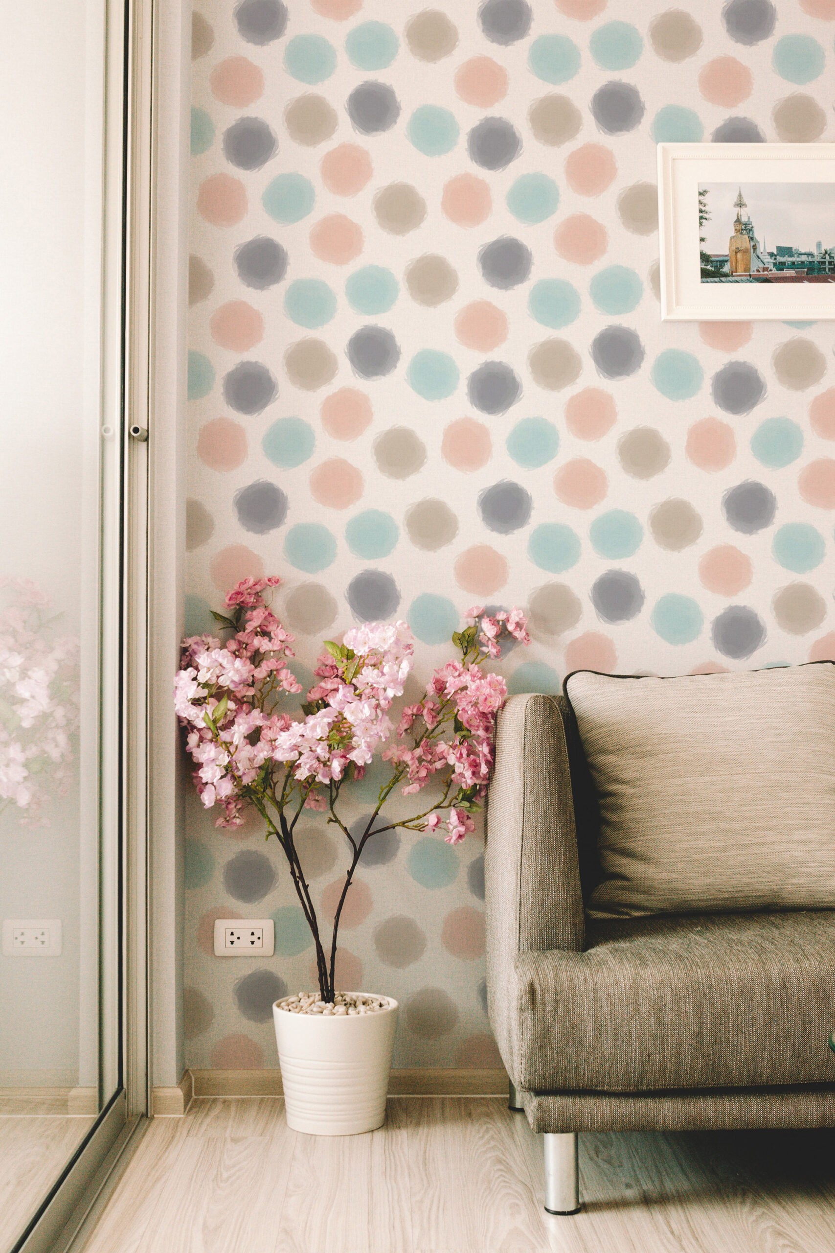 Spaced Beige Dots peel and stick wallpaper in soft pastel circles on a wall beside a sofa in a living room corner.