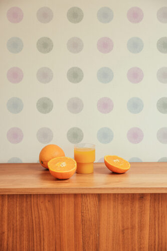 Fine Ivory Sunburst Dots peel and stick wallpaper with pastel sunburst circles on ivory, shown above a wooden sideboard.