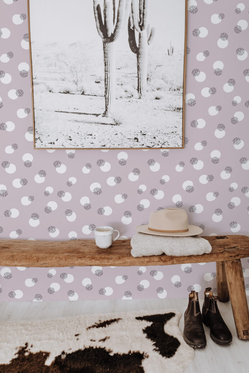 Bold Dusty Rose Dots peel and stick wallpaper with scattered white circles and black speckled dots behind a wooden bench.