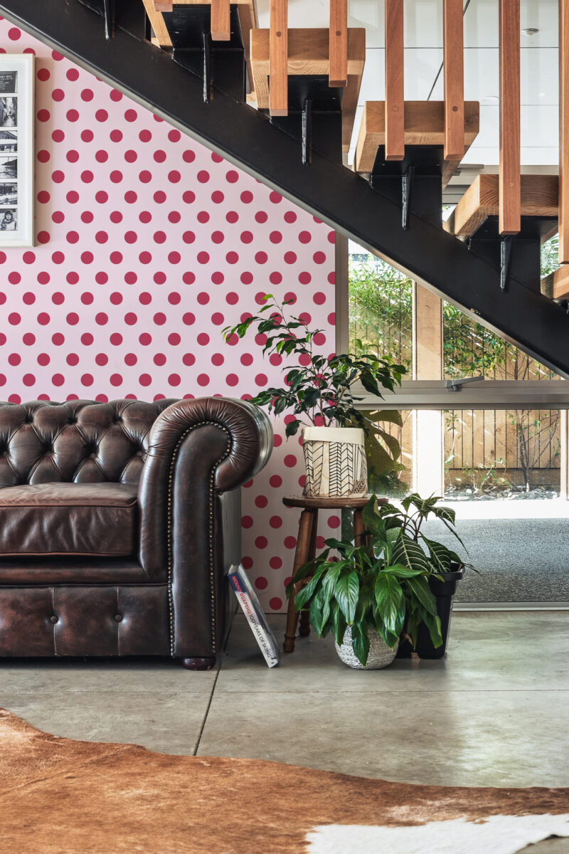 Retro Pink Polka Dot peel and stick wallpaper covers an accent wall beneath the staircase with bold pink dots on pale pink.