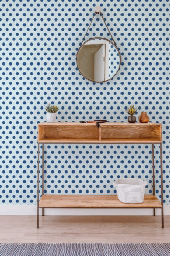 Blue Retro Polka Dot peel and stick wallpaper covering a full wall behind a wood console table and round hanging mirror.