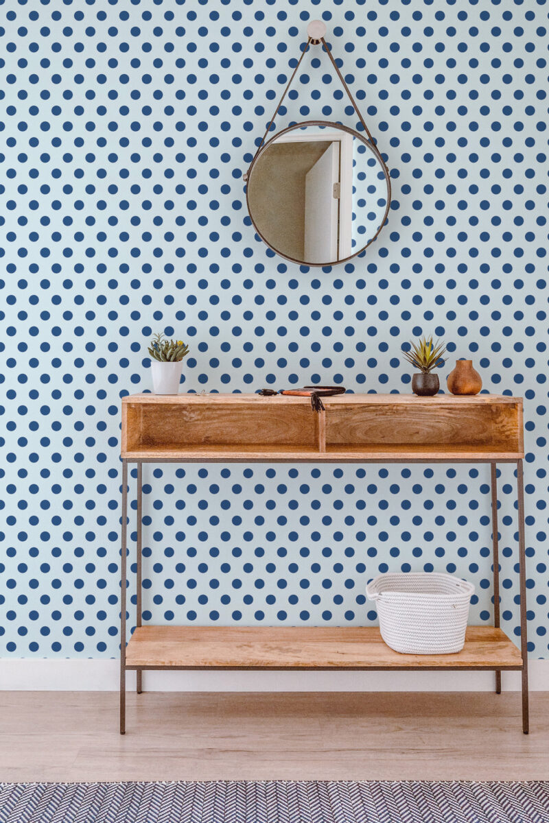 Blue Retro Polka Dot peel and stick wallpaper covering a full wall behind a wood console table and round hanging mirror.