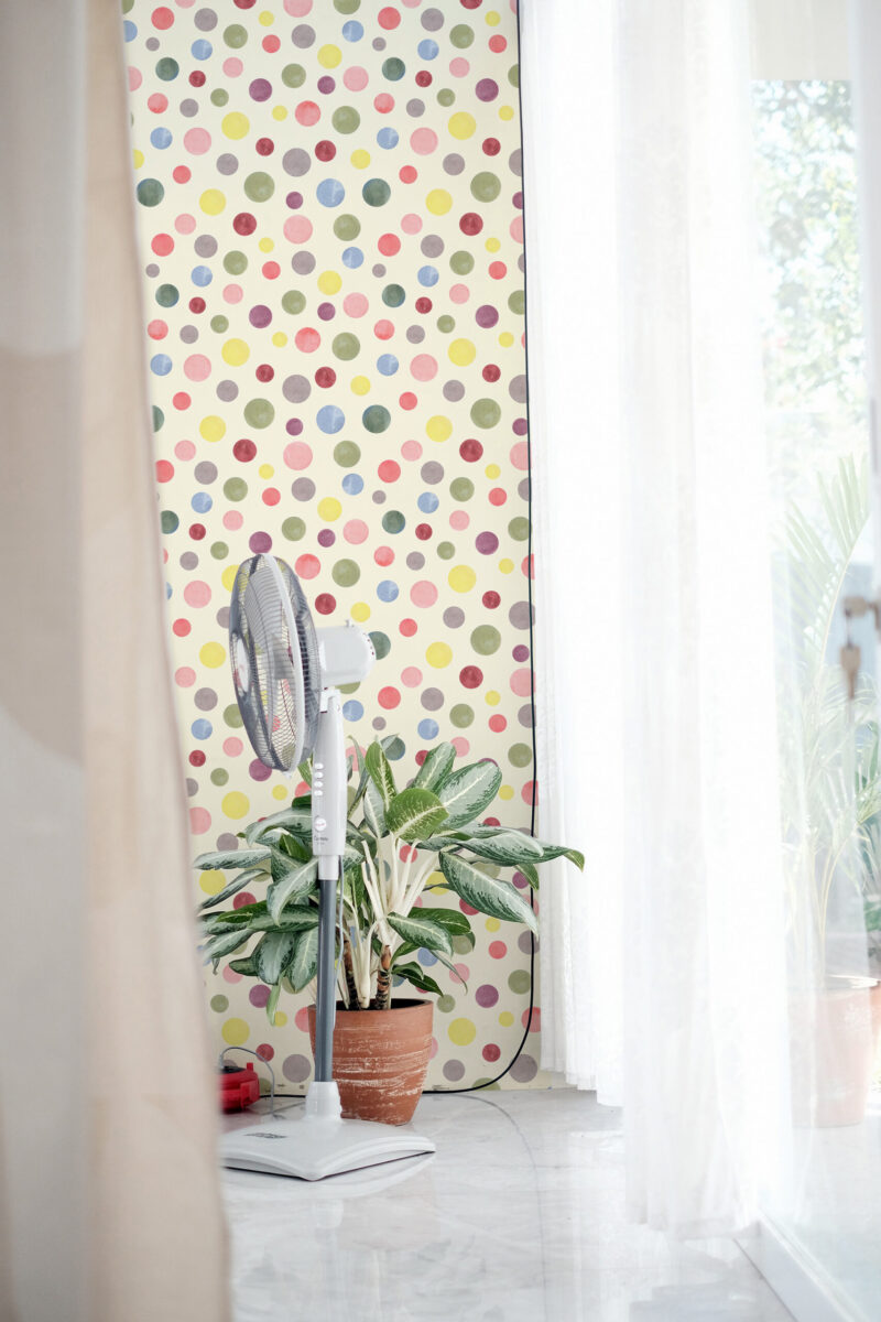Watercolor Cream Polka Dot peel and stick wallpaper with multicolor watercolor dots on a tall wall beside a bright window.