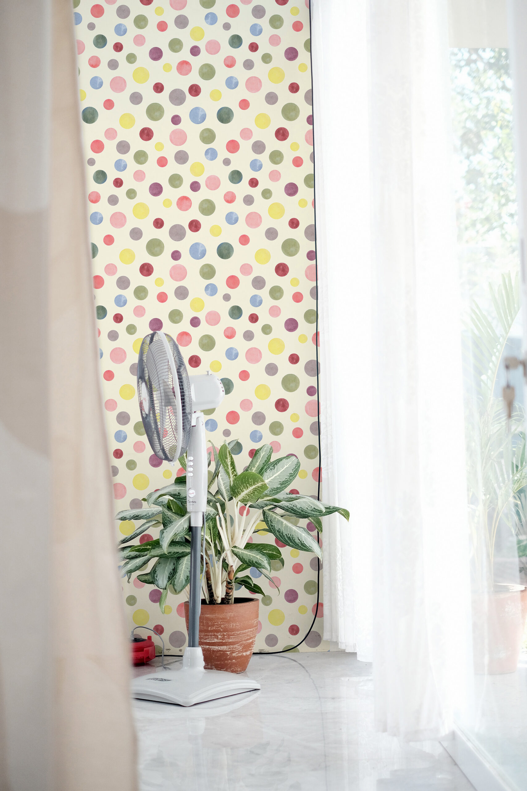 Watercolor Cream Polka Dot peel and stick wallpaper with multicolor watercolor dots on a tall wall beside a bright window.