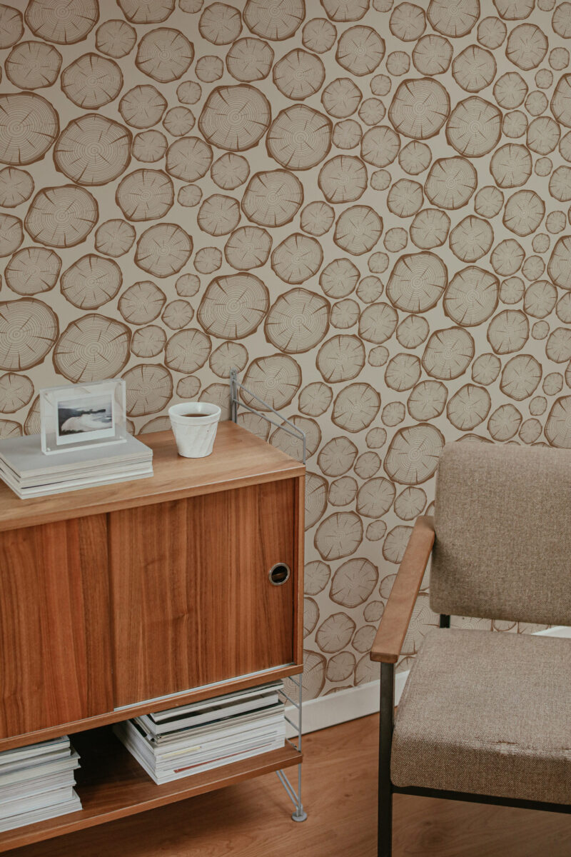 Bold Beige Wood Slice Look peel and stick wallpaper with scattered tree ring slices behind a chair and wood sideboard.