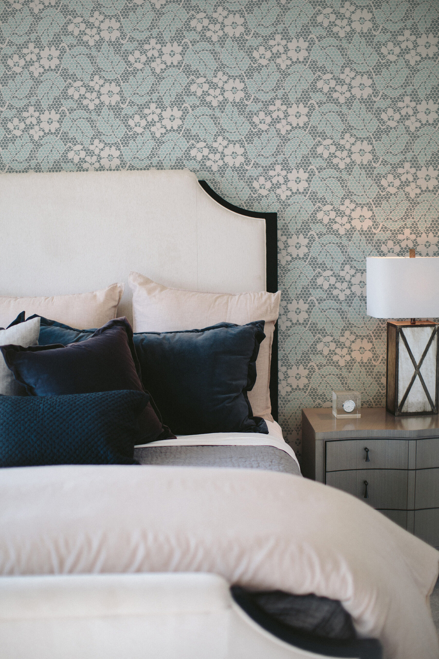 Fine Blue Lace Floral peel and stick wallpaper behind a bed, showing a pale blue lace-like floral pattern across the wall.