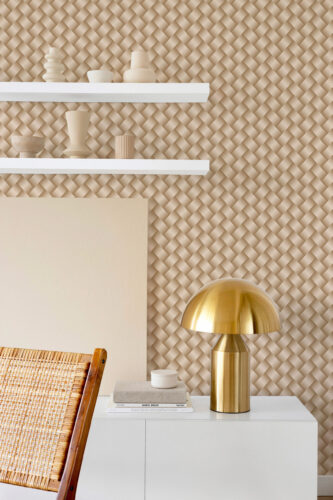 Beige Art Deco Braided Look peel and stick wallpaper with a woven basket-like pattern behind white shelves and a brass table lamp.