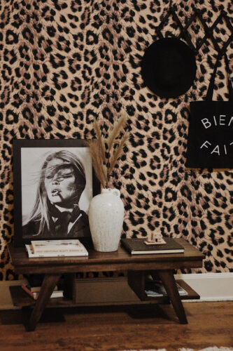 Bold Leopard Print Imitation peel and stick wallpaper in tan and black animal print, shown above a console table with decor.